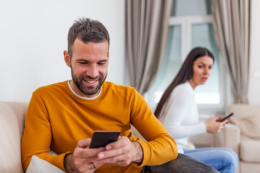 man-texting-his-girlfriend-with-wife-in-the-same-room